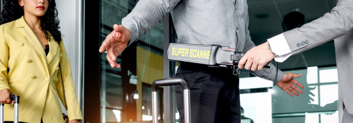 Security man holding metal weapon detector scanner for checking male passenger who going through procedure of physical inspection at entrance airplane gate. Airport security check before flight.