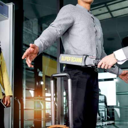 Security man holding metal weapon detector scanner for checking male passenger who going through procedure of physical inspection at entrance airplane gate. Airport security check before flight.