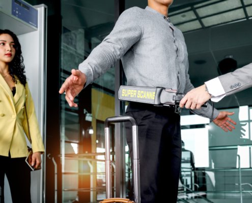 Security man holding metal weapon detector scanner for checking male passenger who going through procedure of physical inspection at entrance airplane gate. Airport security check before flight.